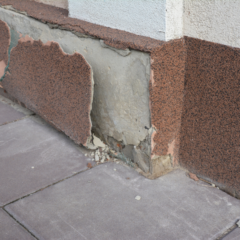 A damaged stucco foundation, basement because of bad waterproofing and wetness. A close up of a slipped, cracked stucco, fallen parging on the basement outside the house. - stock photo