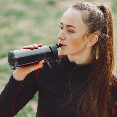Woman in black sweater drinking from a black reusable water bottle.