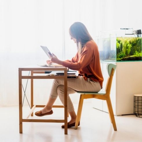 Female freelancer working at home sitting at desk using tablet with aquarium