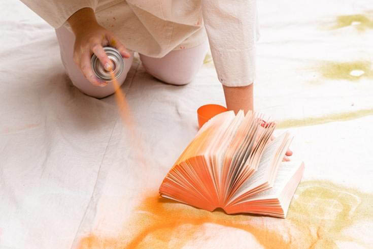 Tiffany Pratt spraying a paperback book with orange paint