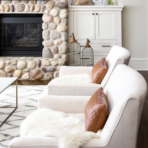 two ivory chairs with tan cushions and white fur throws in front of fireplace