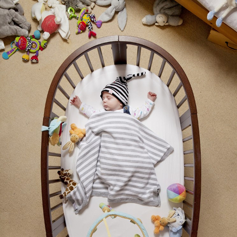 A baby sleeps in a cluttered nursery with toys on the floor