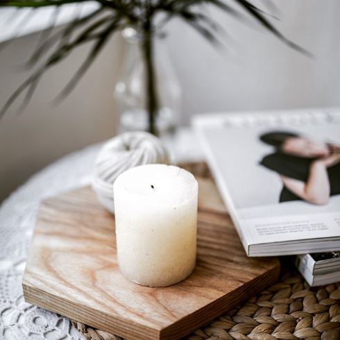A large pillar candle on a wooden tray in a soft-coloured room
