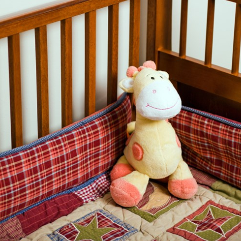 A baby crib with soft bumper and stuffed toy