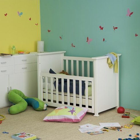 A drop-side crib in a green and yellow nursery room