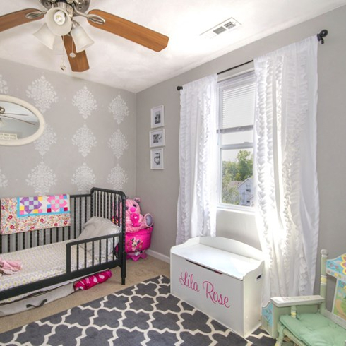 A baby nursery with an overhead light, white crib, and carpet