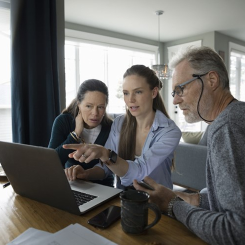 parents and adult daughter look at laptop in kitchen
