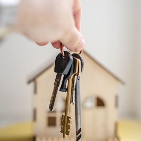 A person holding a set of keys in front of a small toy house