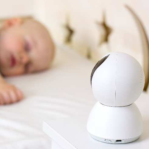 Cute little baby boy sleeping on bed at home with baby monitor camera. - stock photo