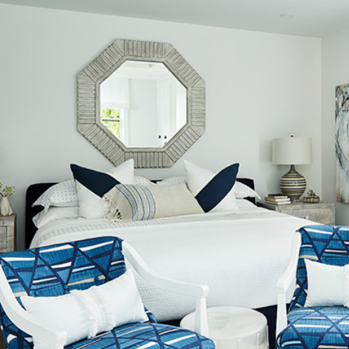 A white bedroom with blue furniture and mirror above the headboard