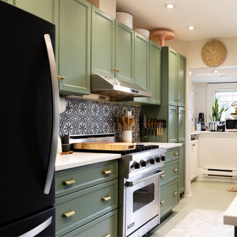 A narrow renovated kitchen with green cabinetry and wood open shelving