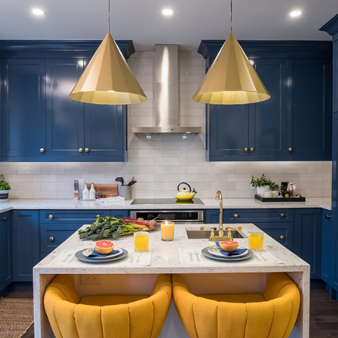 A blue and yellow renovated kitchen with minimal counter clutter and unique lighting