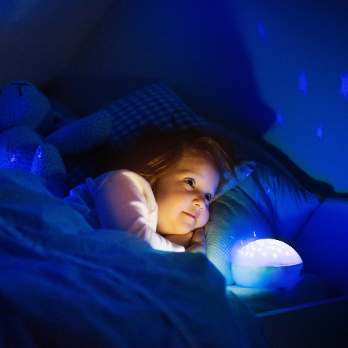 Little girl in bed with night lamp in dark nursery - stock photo