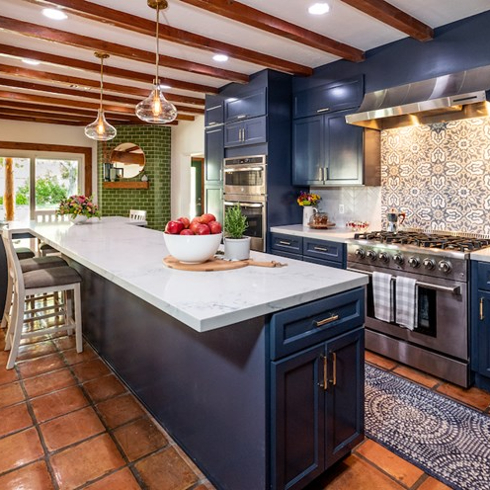 Charming large kitchen with navy blue cabinets, geometric blue and grey tile backsplash, stainless steel appliances, white quartz island, terra cotta tile floors and exposed beams on the ceiling