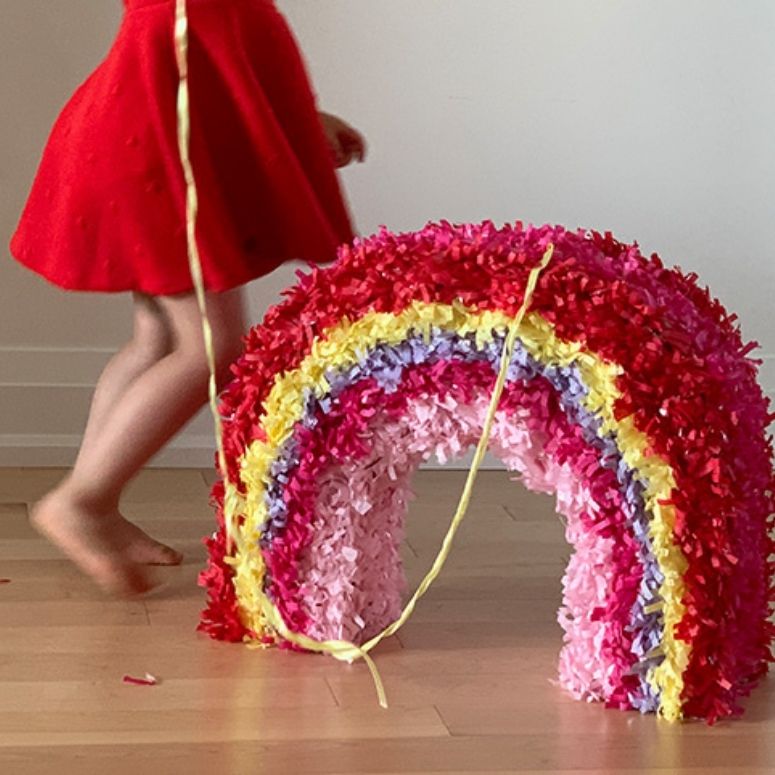 Rainbow pinata on the ground, and a girl in a red dressing running behind it.