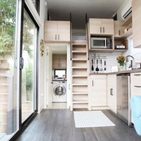 interior of a tiny house with large glass windows, showcase the kitchen, part of the living room and loft bedroom