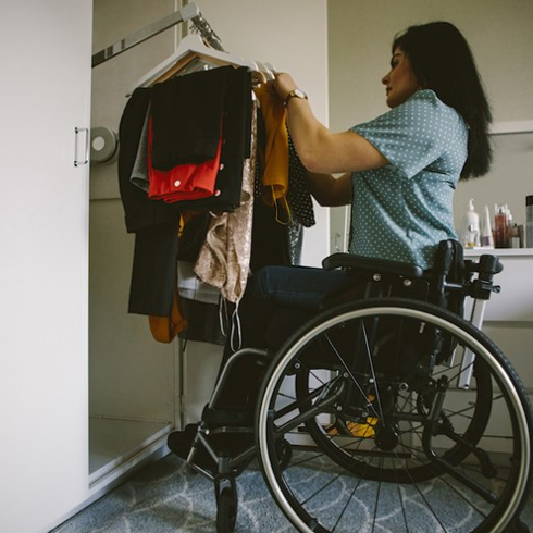 Full length side view of young disabled woman looking at clothes hanging in wardrobe