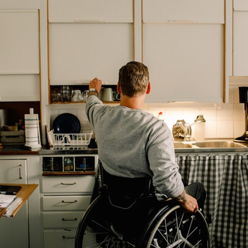 disabled man opening cabinet in white kitchen at home