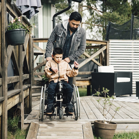 man pushing child sitting on wheelchair in yard