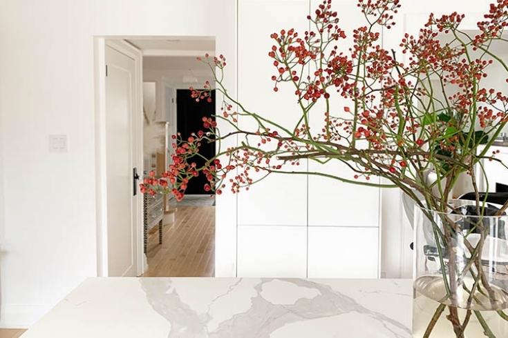 Branches in a glass vase with red faux flowers, placed on a white kitchen counter.