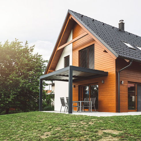Wood-front house with a black roof, black trim and a black porch overhang, situated on a large grassy property.