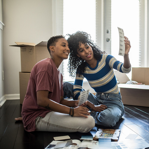 Black female couple sitting on the floor of an empty home, discussing renovations.