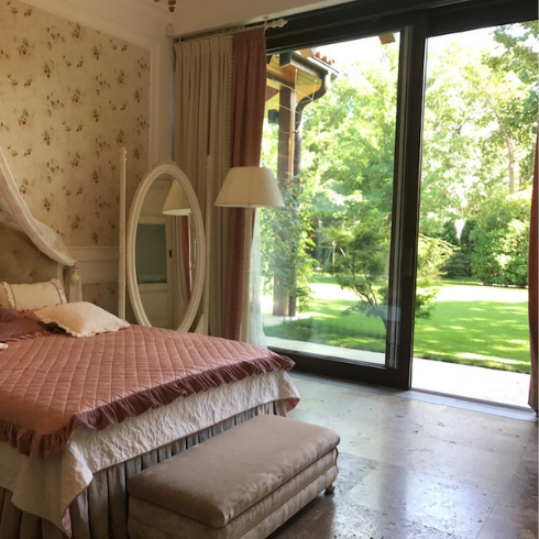 pink bed in wallpapered bedroom with sliding door to green yard