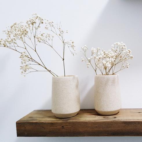 Wooden wall shelf with two white vases and flowers.