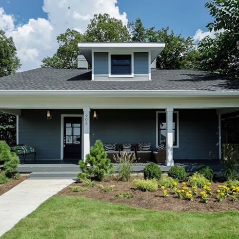 Exterior of a beautiful blue and white bungalow with large front porch with pillars and outdoor seating, a well-manicured front lawn and attractive landscaping as featured on Master of Flip on HGVT Canada