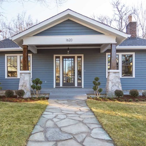 Exterior of a cute blue and white bungalow with a wide flagstone path, lawn and landscaped garden beds as features on Masters of Flip on HGTV Canada