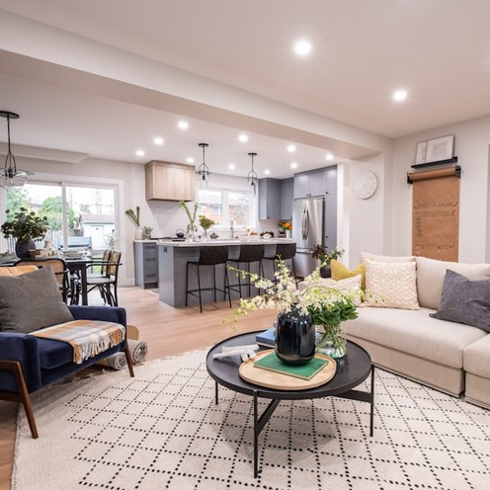 Beautiful open concept living room with a large cream coloured sectional couch, a round black coffee table, a large geometric white rug, a navy blue mid-century modern velvet armchair, looking into a grey kitchen as features on Property Brothers Forever Home on HGTV Canada