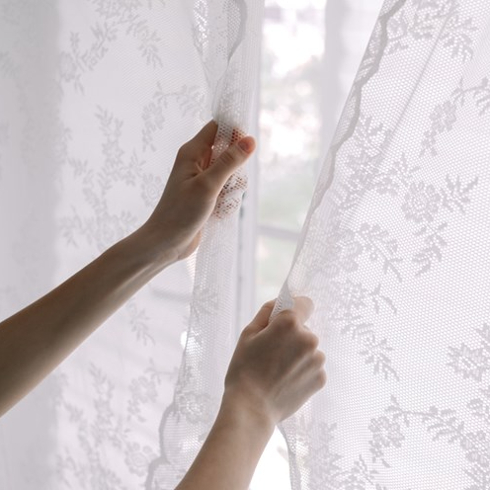 Woman closes lace curtains in bedroom, close-up. Domestic life