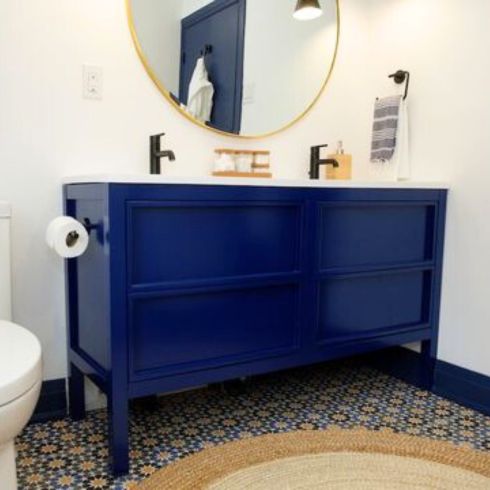 white bathroom with round mirror, blue vanity and small glass storage containers