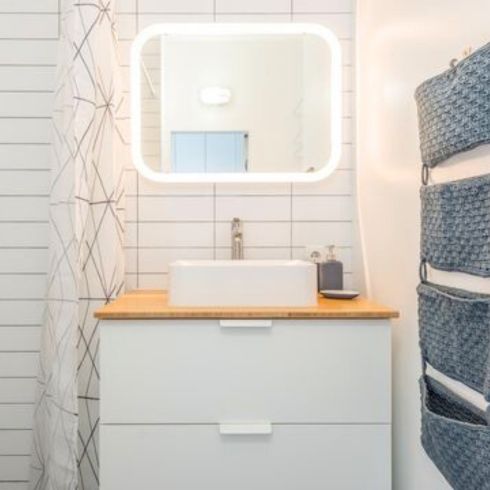 modern white bathroom with lighted mirror and tiered hanging storage piece