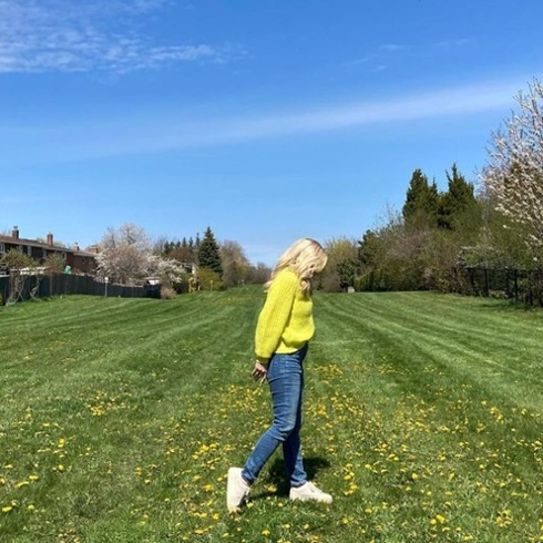 Kortney Wilson in a yellow sweater and blue jeans in a field of yellow flowers