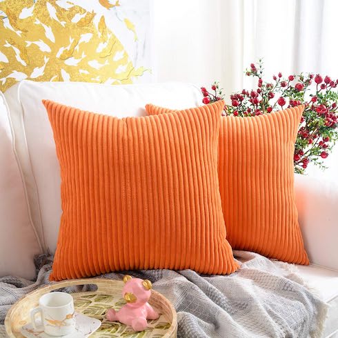 Two orange corduroy throw pillows on a cozy white couch