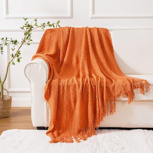 A cozy orange throw blanket draped on a white couch