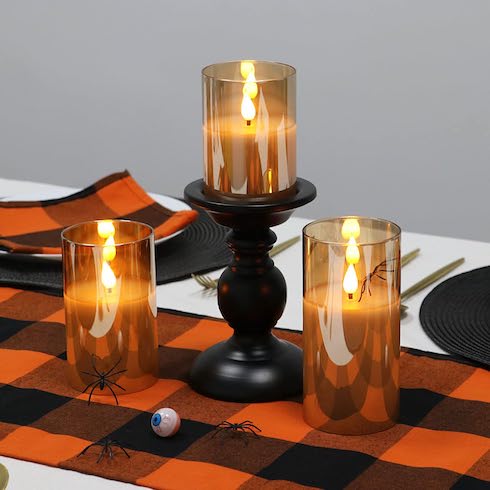 Three flameless candles on an autumn tablescape featuring Halloween decorations and an orange-and-black table runner