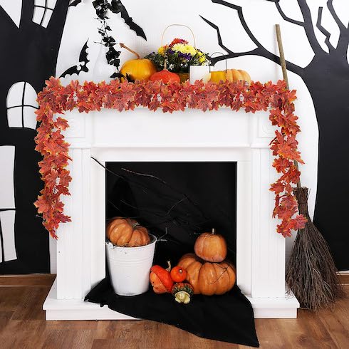 A white fireplace decorated for fall with a mix of pumpkins and an orange maple-leaf-themed garland