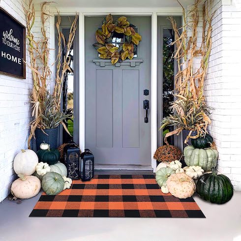 A blue front door surrounded but fall decor including a mix of decorative pumpkins and an orange-and-black front doormat