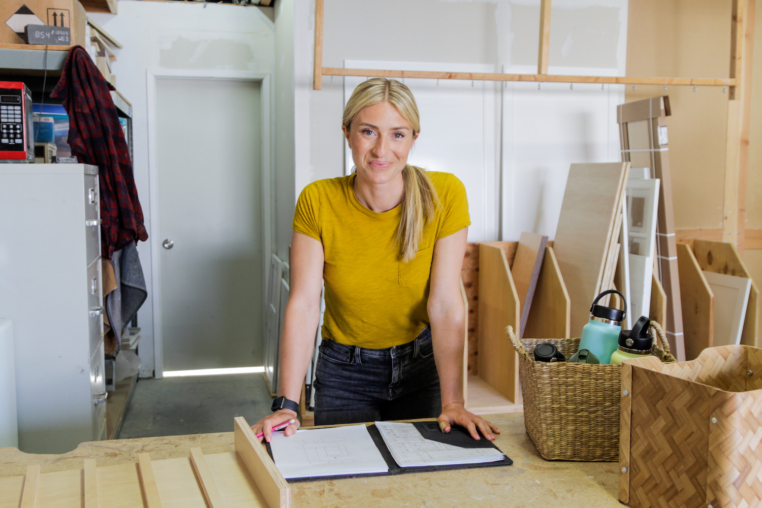 Jasmine Roth Blonde smiling woman in yellow t-shirt and jeans standing in a home under renovation