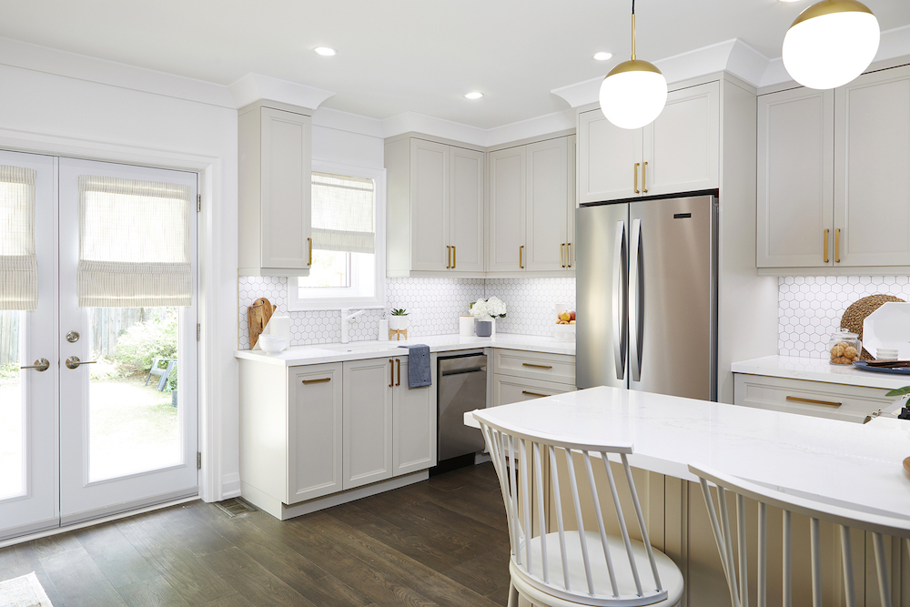 Gorgeous smoky white cabinets with gold hardware are featured in a kitchen designed by Samantha Pynn and Sebastian Clovis in this Save My Reno kitchen featured on HGTV