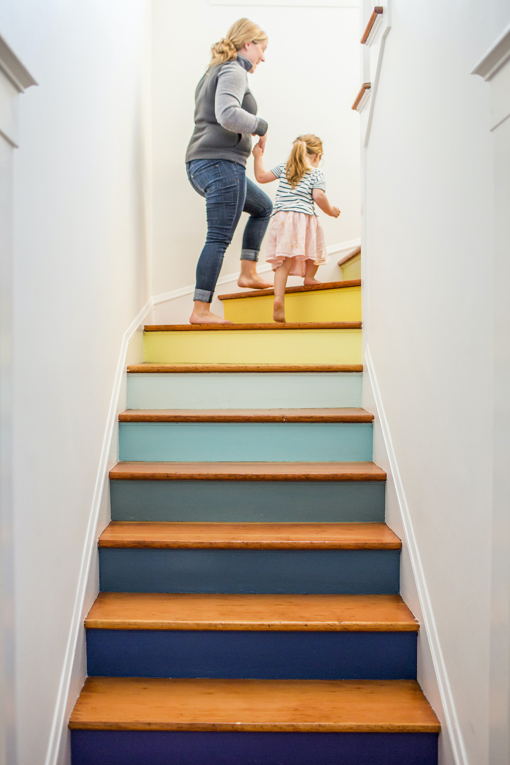 Mother and daughter holding hands climbing a multicolour wooden staircase painted with blue, green and yellow paints of various shades