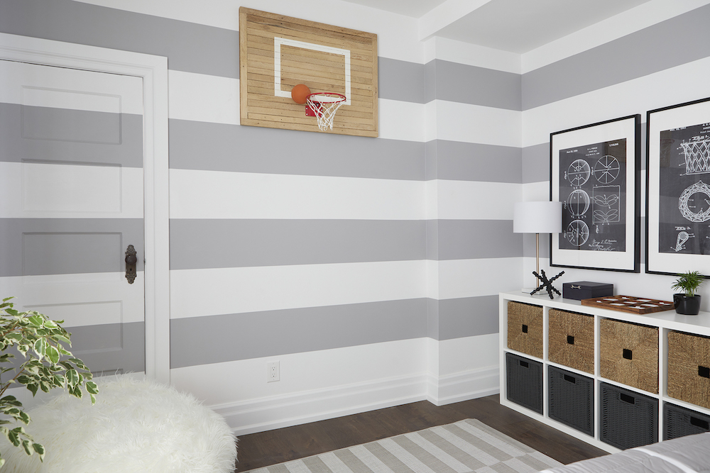 Cool kids room with a white consul with square baskets, white and grey painted stripes on the wall, and a toy basketball hoop designed by Sebastian Clovis and Samantha Pynn on Save My Reno shown on HGTV Canada