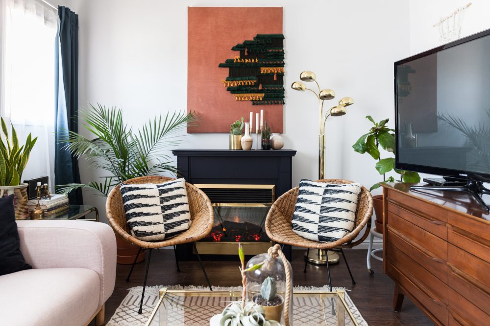 two wicker chairs with black and white cushions in front of black fireplace and brass floor lamp