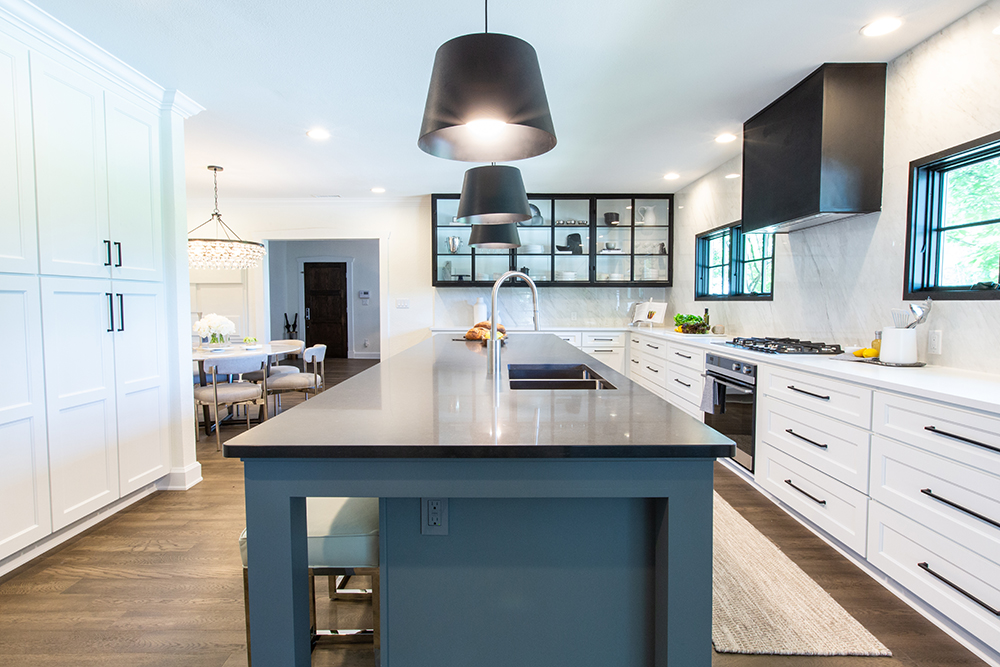 Beautiful new kitchen with large blue centre island with grey countertop, lots of white cabinets with crown moulding, and a long white L-shaped quartz countertop
