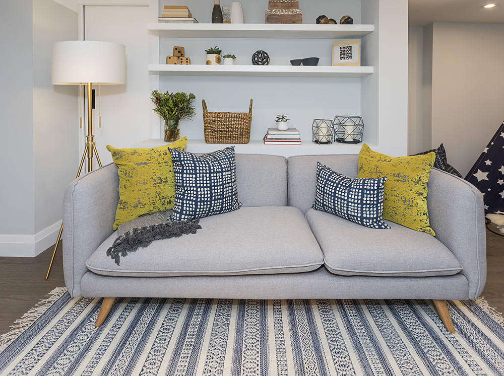 Chic grey couch with yellow and blue throw cushions and patterned blue and white rug