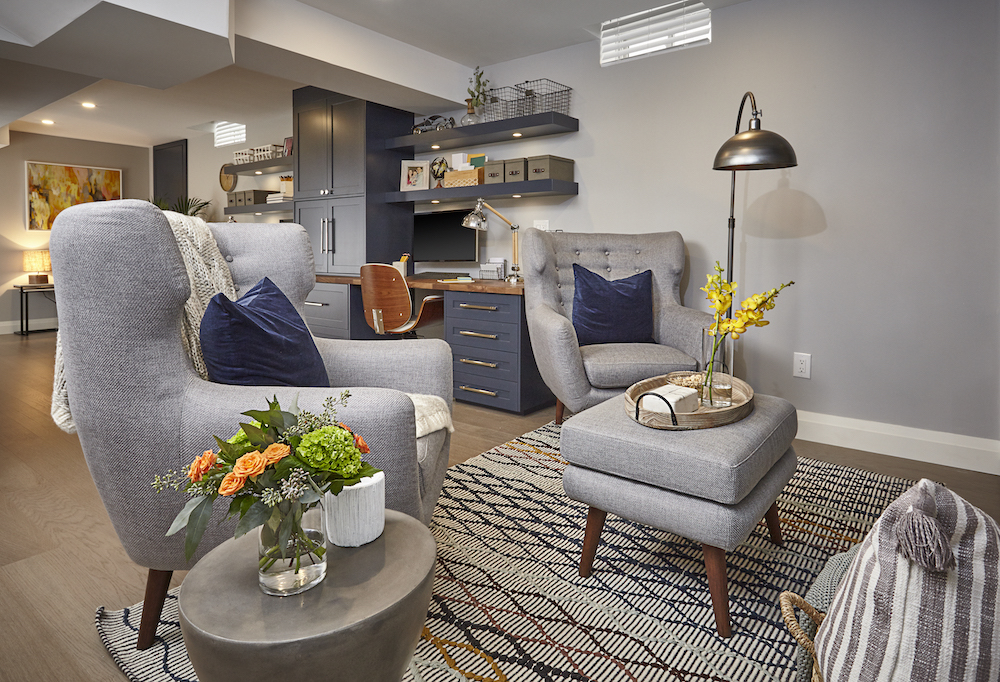 Chic basement living area with two grey armchairs, a grey ottoman, silver side table and a patterned rug