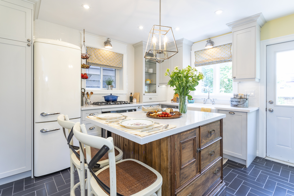 Charming renovated kitchen with wooden centre island, white cabinets and countertops and retro-inspired fridge