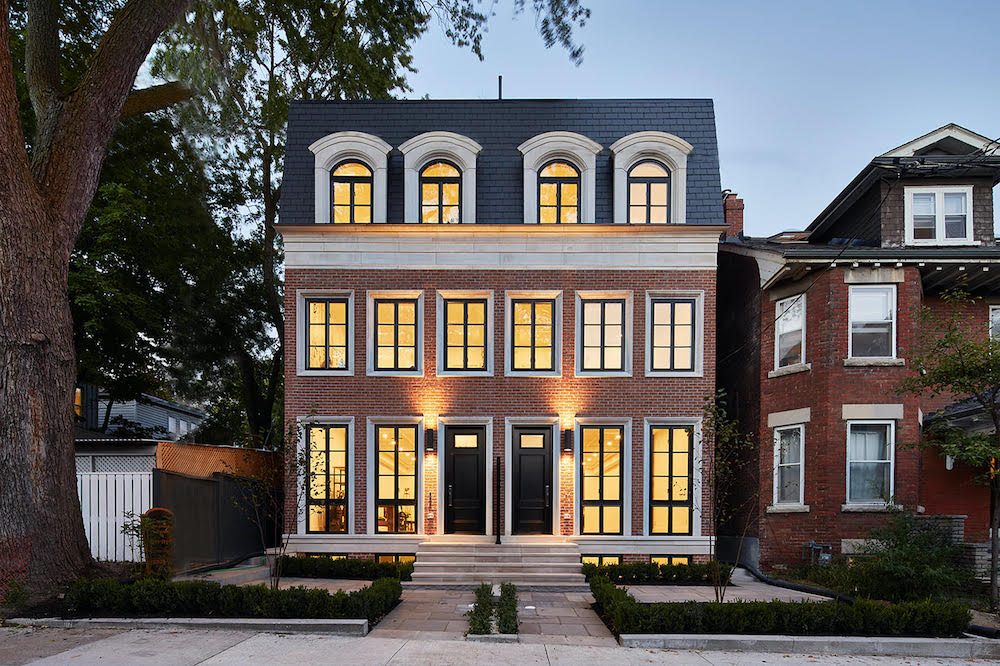 Exterior of a beautiful brick house at dusk with all the black framed windows lit up with interior lights
